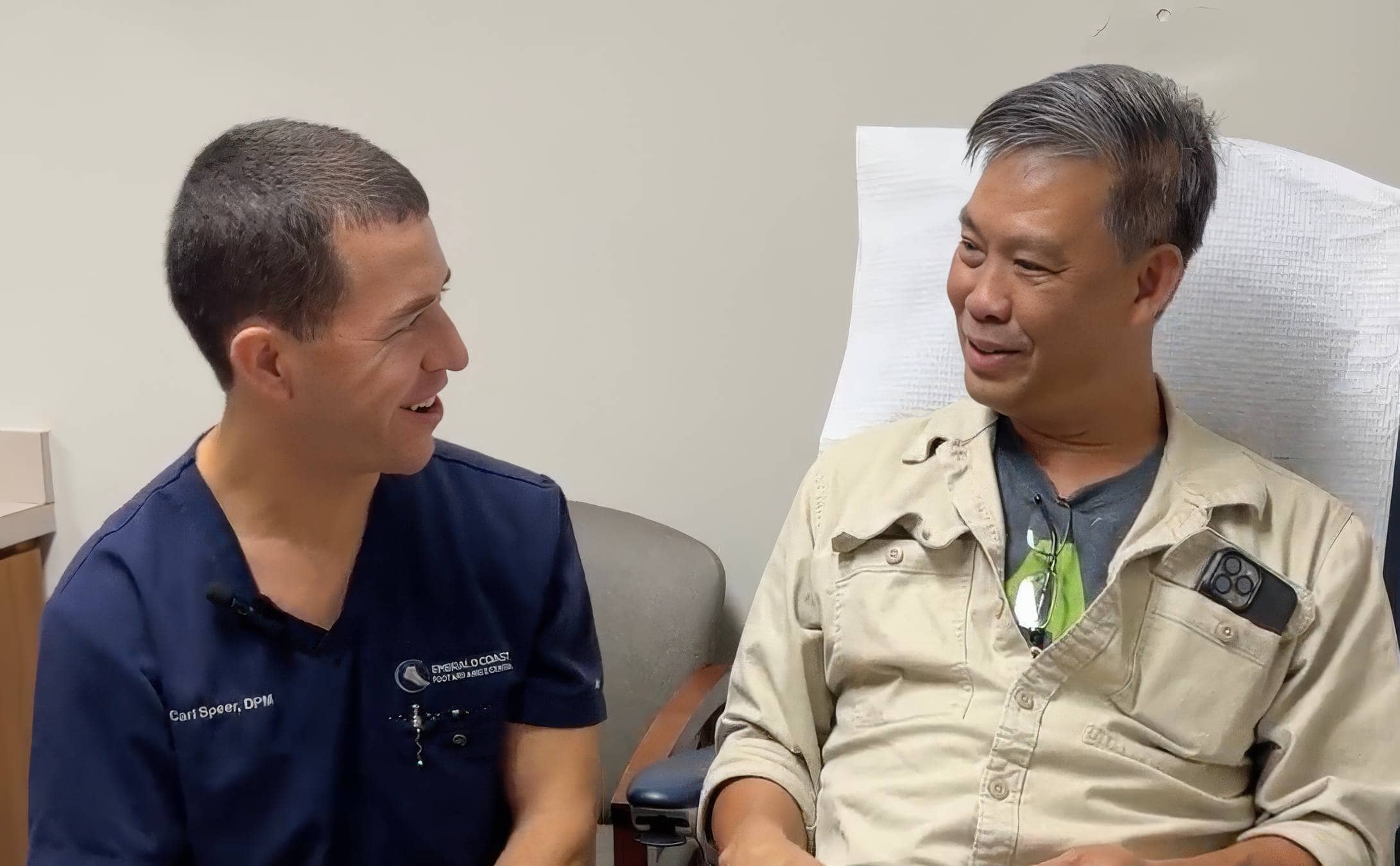 Doctor and patient smiling and conversing in a medical office, illustrating positive post-surgery experience at Emerald Coast Foot and Ankle Center.